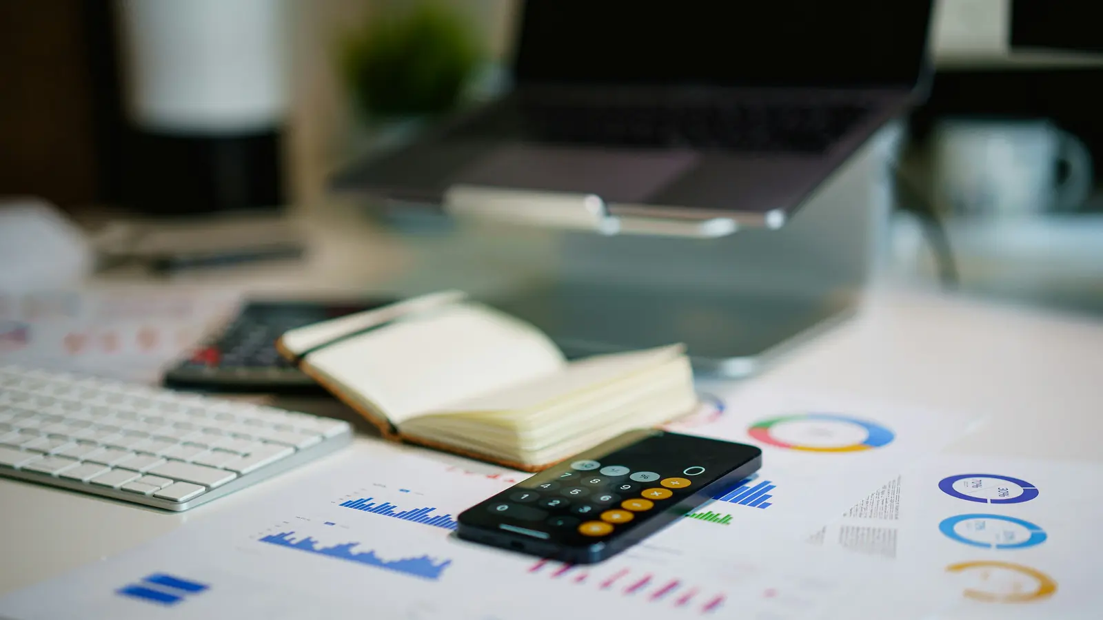 Laptop, calculator, notebook and printed charts arranged for checking digital business records